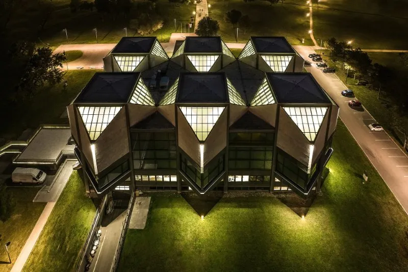 An aerial view at night of the Museum of Contemporary Art in Belgrade, a building with six lit, pointed glass skylights on a dark lawn.