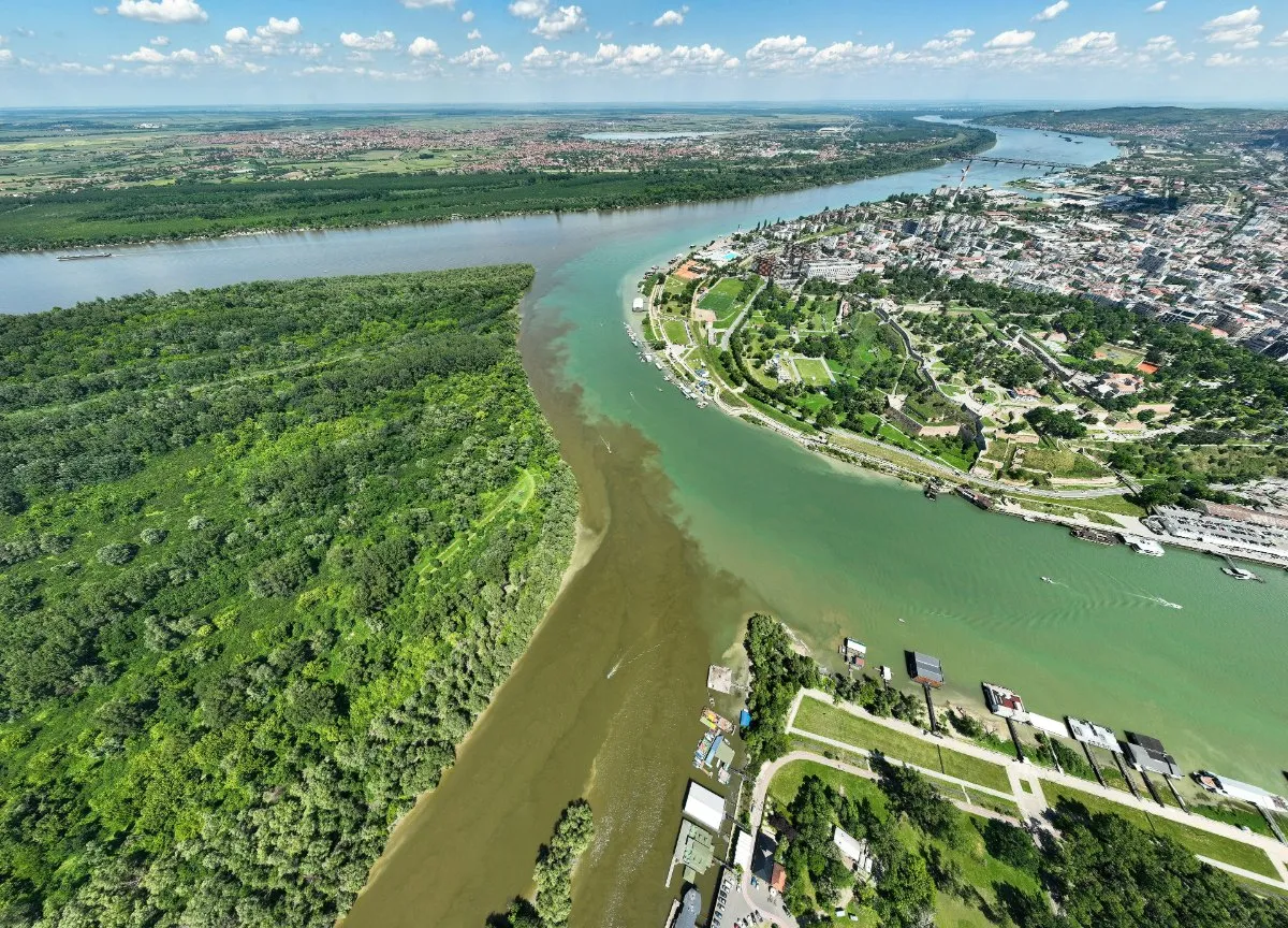 An aerial view of the green Sava flowing into the wider Danube, with the Kalemegdan park and the old town of Belgrade on the right bank and the wooded Great War Island on the left.