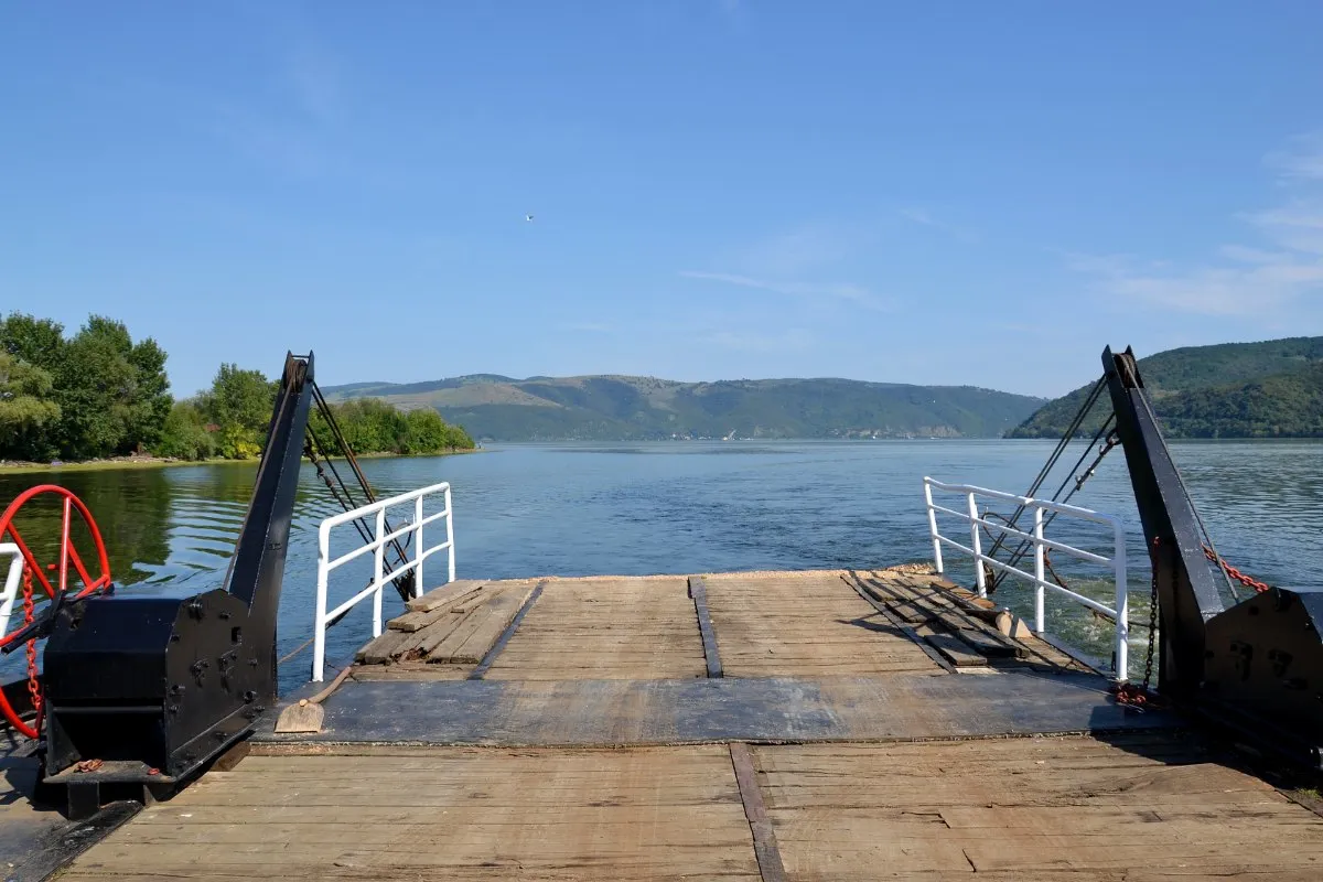 The wooden deck and raised ramps of a small ferry on the wide Danube between Ram and Stara Palanka, with green hills on the far bank.